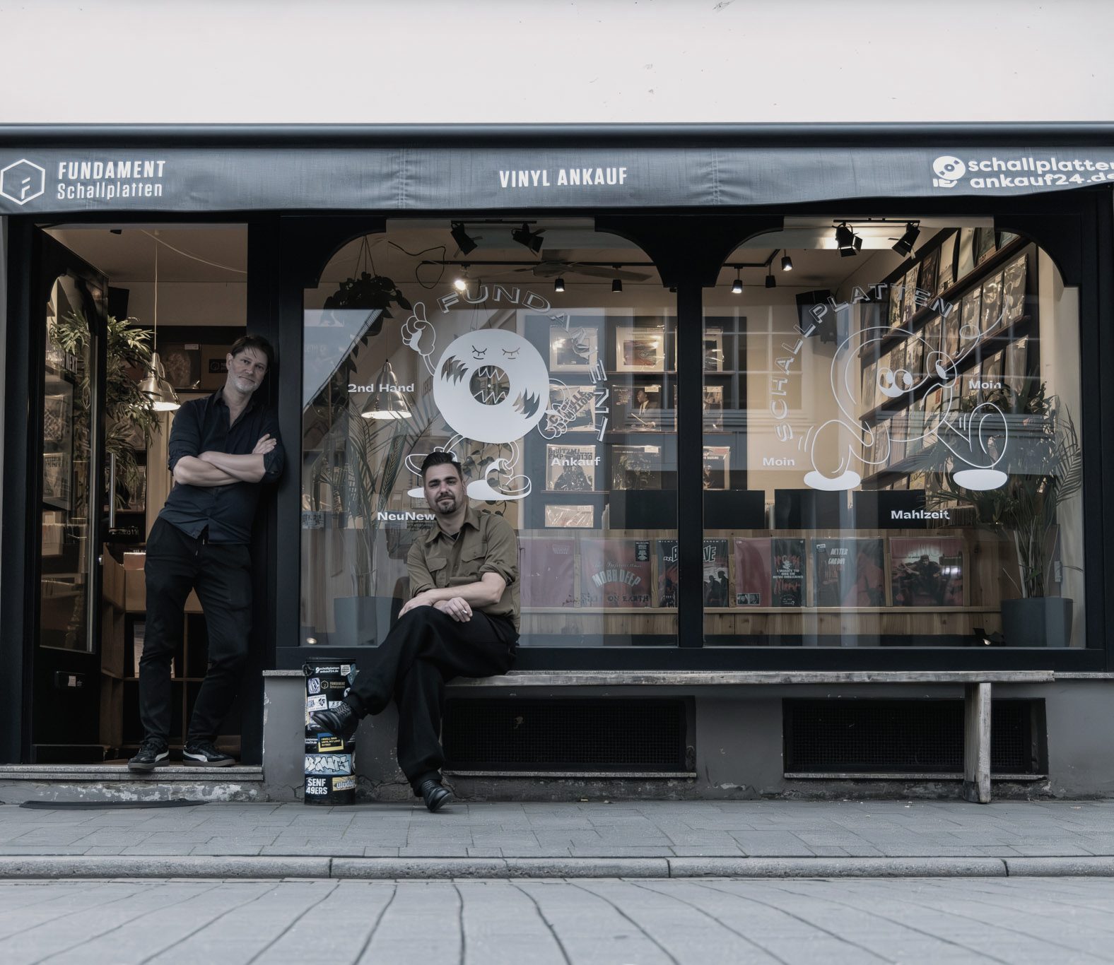 Ladenfront von FUNDAMENT Schallplatten mit Markise und Schaufenster, davor die beiden Inhaber.